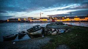 Escena costera con barcos, una grúa y edificios a lo largo de la orilla.