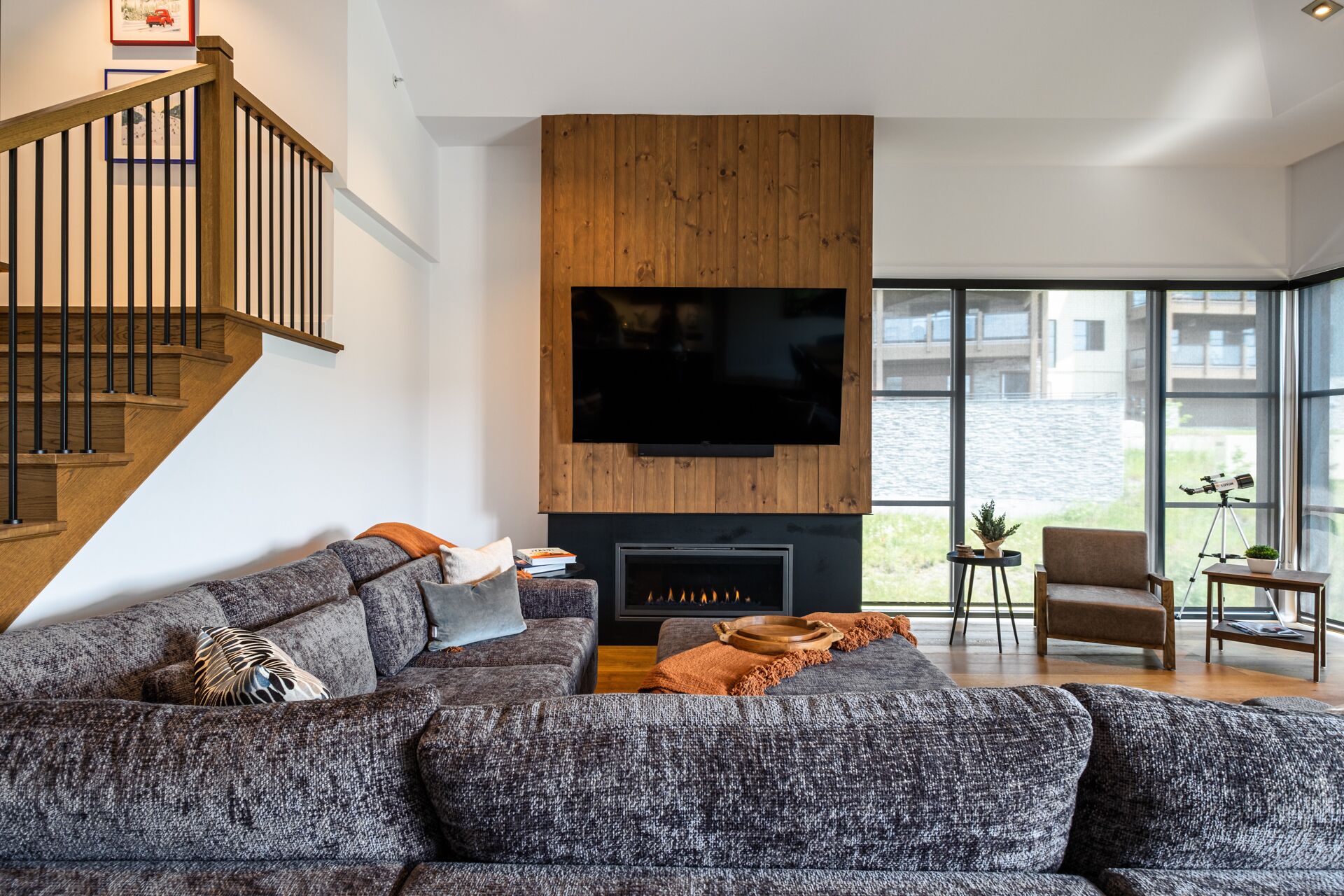 Ein modernes Wohnzimmer mit Kamin, großem Flachbildfernseher, einer Couch und einer Treppe.