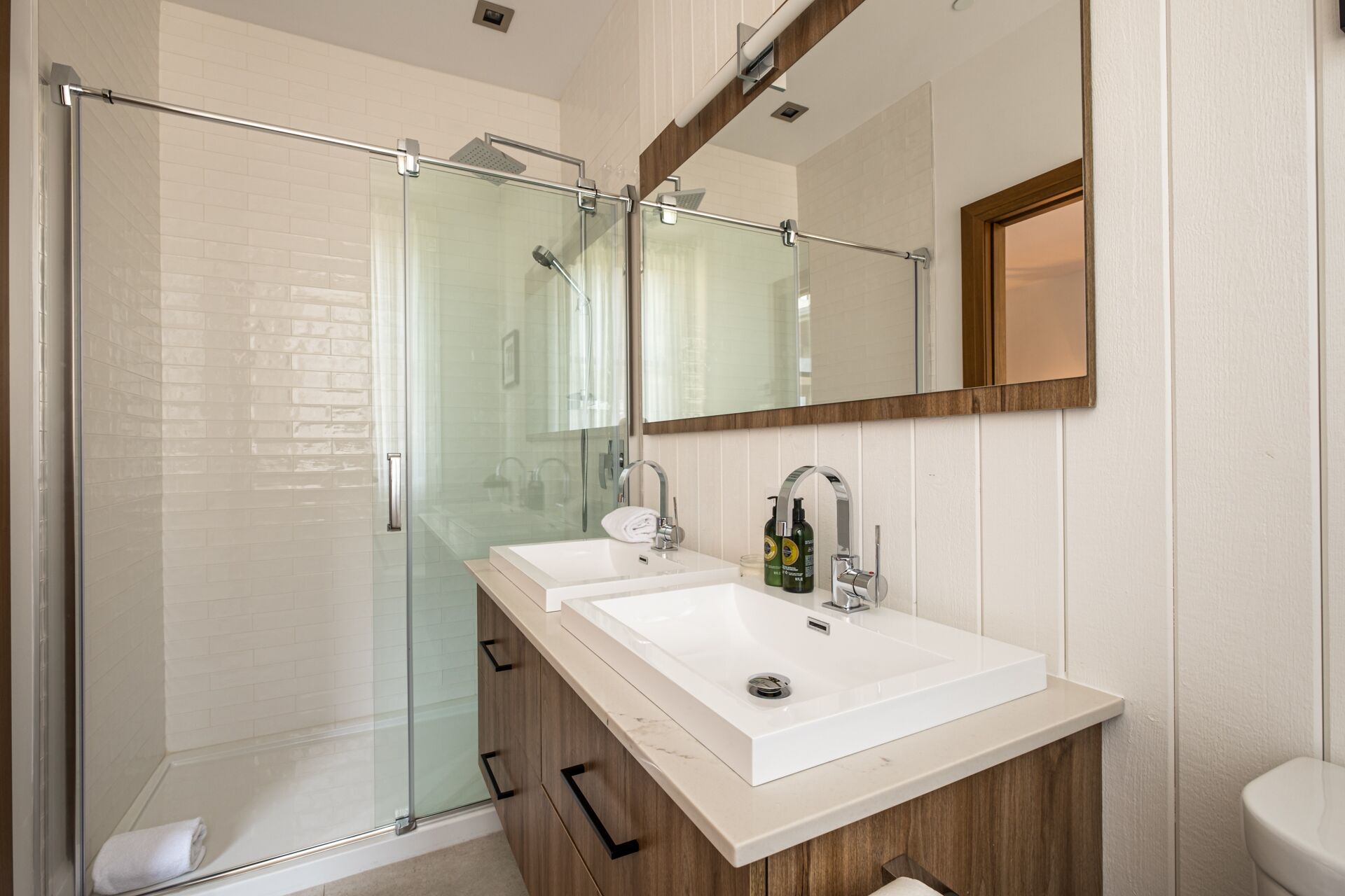 A modern bathroom with a glass shower enclosure, a double sink vanity, and a large mirror.