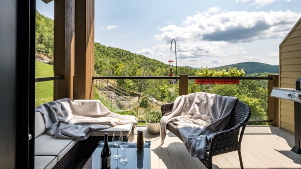 Ein Balkon mit zwei Korbstühlen, einem Tisch mit Flasche und Gläsern sowie einem Grill.