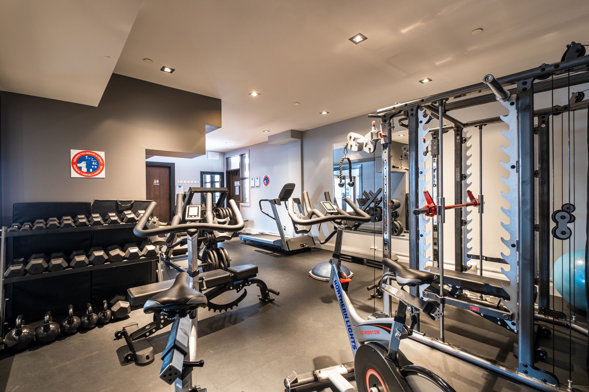 Ein Fitnessstudio mit verschiedenen Trainingsgeräten, darunter Kurzhanteln, Laufbänder und Kraftmaschinen.