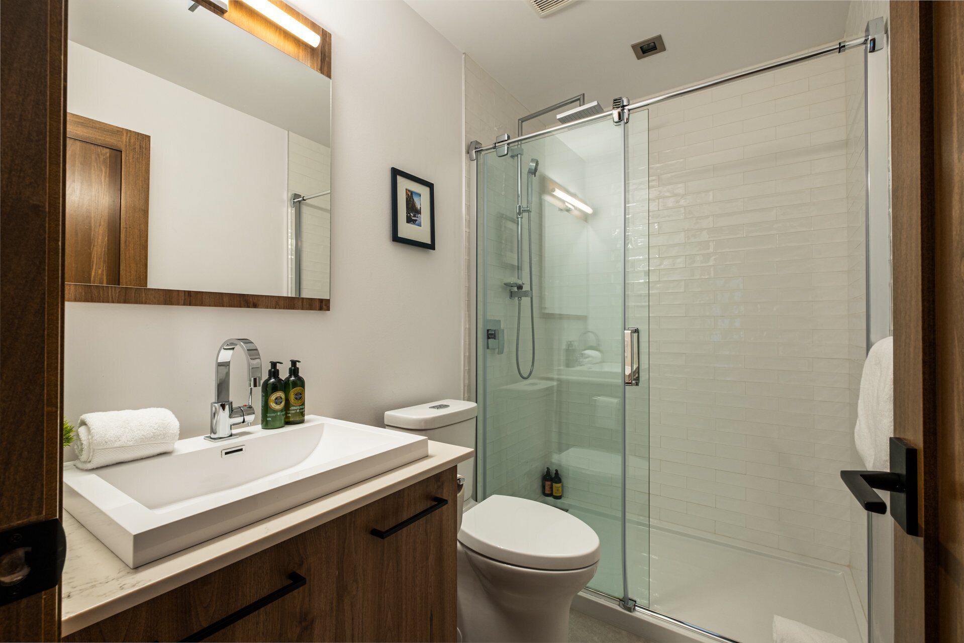 A modern bathroom with a glass-enclosed shower, a wooden vanity, and a white toilet.