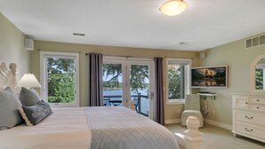 Un dormitorio con cama, cómoda, televisor y balcón con vista a árboles.