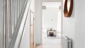 A hallway with a staircase, a dining area with a table and chairs, and a radiator on the wall. - Deluxe 2 Bed Flat with Balcony in Hackney (London)