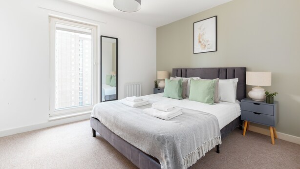 A bedroom with a bed, bedside tables, a window, and a ceiling light. - Deluxe 2 Bed Flat with Balcony in Hackney (London)