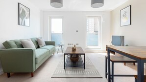 A modern living room with a green sofa, a wooden coffee table, and a dining table. - Deluxe 2 Bed Flat with Balcony in Hackney (London)