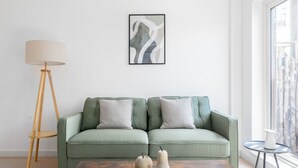 A living room with a green sofa, two decorative vases, a floor lamp, and a framed abstract painting on the wall. - Deluxe 2 Bed Flat with Balcony in Hackney (London)