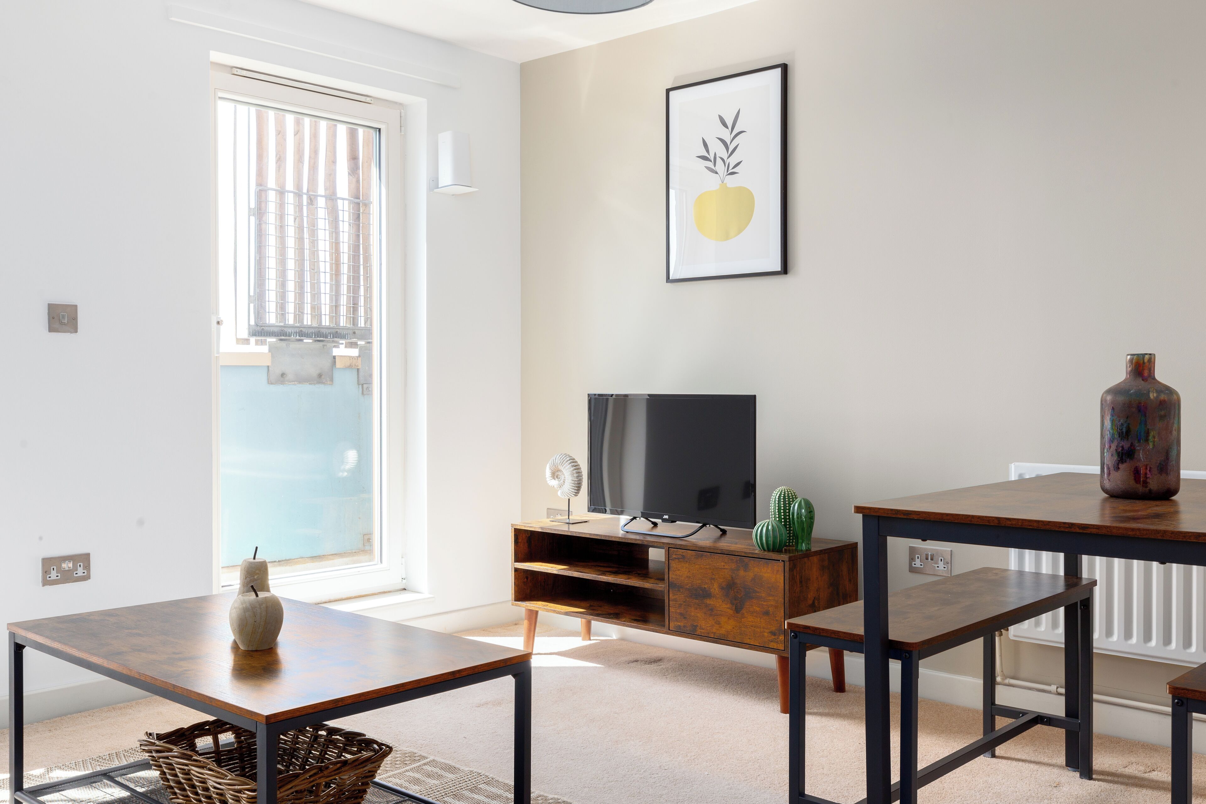 Un salon avec un téléviseur, une table, un banc, un cactus et un tableau encadré au mur.