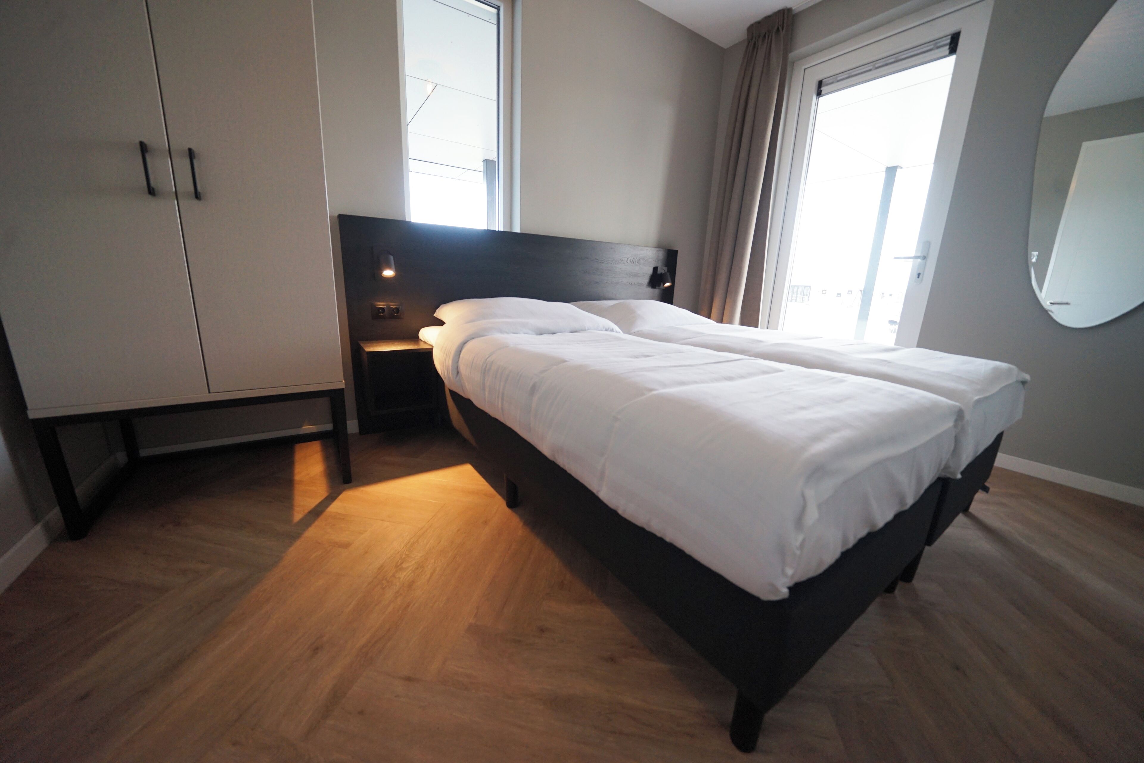 Een moderne hotelkamer met een groot bed, een kledingkast, een nachtkastje en een raam met gordijnen.