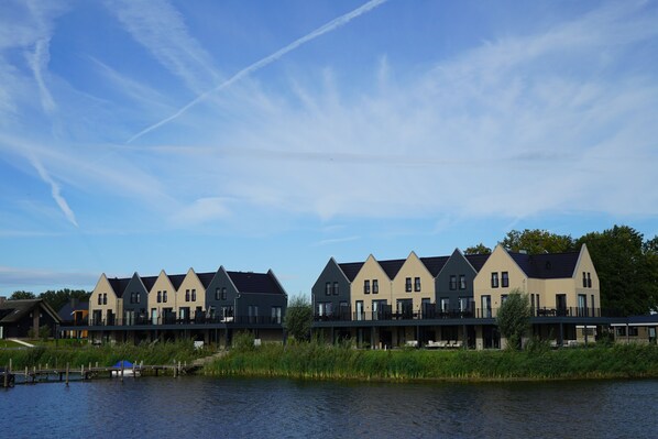 Een rij moderne, meerlaags huizen met balkons, gelegen aan een rustig waterlichaam, waarschijnlijk een meer of rivier.