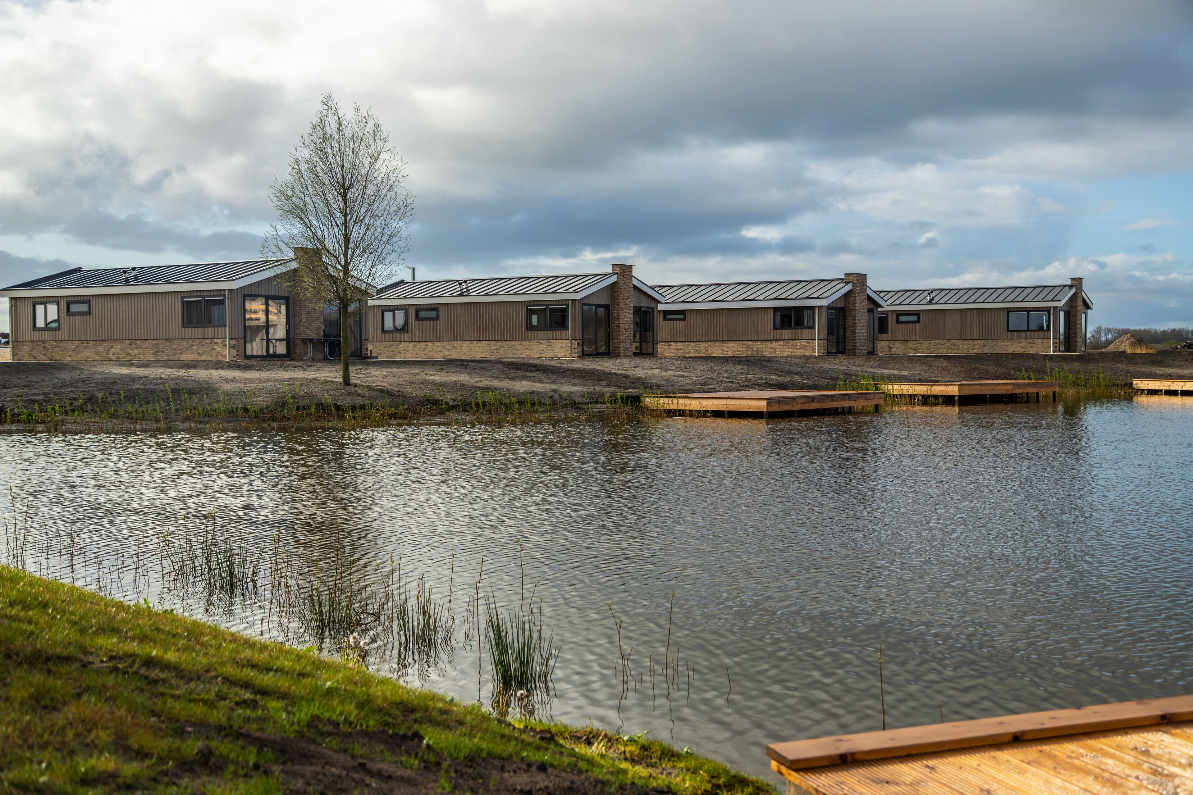 A modern building with a flat roof and large windows, situated next to a calm body of water with wooden docks.
