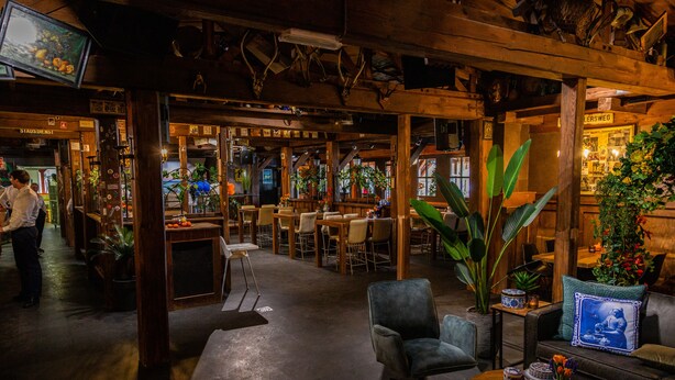 Un interior acogedor con vigas de madera, una zona de bar y diferentes disposiciones de asientos.