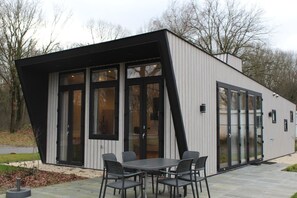 En moderne bygning med et unikt, kantet design, store glasvinduer og en terrasse med borde og stole.