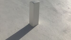 Una terraza en la azotea con piso de concreto, pilares blancos y vistas despejadas de los edificios circundantes.