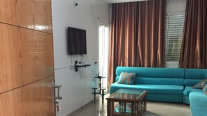 Una sala de estar con un sofá color turquesa, un armario de madera, un televisor de pantalla plana y un ventilador de techo.