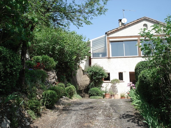 A house with a gravel driveway, surrounded by lush greenery and potted plants.
