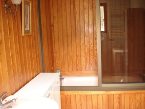 Une salle de bain avec un lambris en bois, un lavabo blanc et une douche à parois de verre.