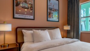 A hotel room with a bed, two bedside tables with lamps, a window with curtains, and two framed pictures on the wall. - 129 · ☀Pool✔ Kitchen✔ Beach✔ Self Checkin✔ Free Parking✔ (Clearwater)
