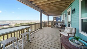 A wooden deck with a view of the beach, outdoor seating, and a house with teal siding. - New Build! Beach Front Luxury House w/Ocean Views & Breeze (Freeport)