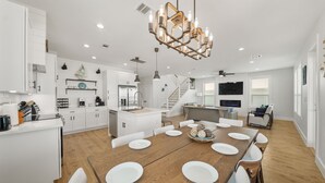 A spacious kitchen with white cabinetry, a wooden dining table set for six, and a modern chandelier. - New Build! Beach Front Luxury House w/Ocean Views & Breeze (Freeport)