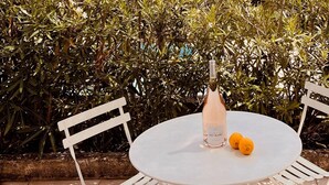 Ein Tisch mit einer Flasche und Obst, umgeben von Grünpflanzen und Blick auf Berg und Meer.
