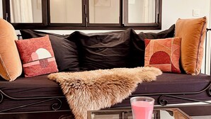 Ein modernes Wohnzimmer mit einem dunklen Sofa, mehreren Kissen, einem Fellüberwurf und einem Glastisch mit einem pinkfarbenen Gegenstand.