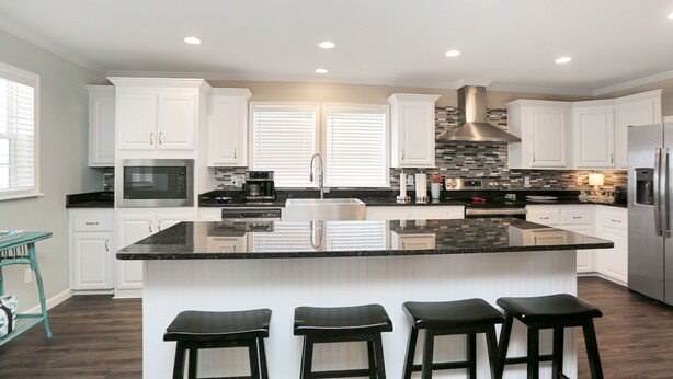 Una cocina moderna con armarios blancos, una isla grande con taburetes, una campana extractora de acero inoxidable y un microondas integrado.