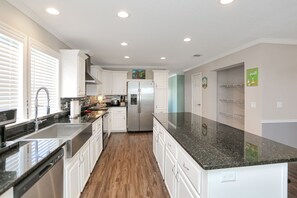 A modern kitchen with white cabinets, a stainless steel refrigerator, and a black granite countertop.