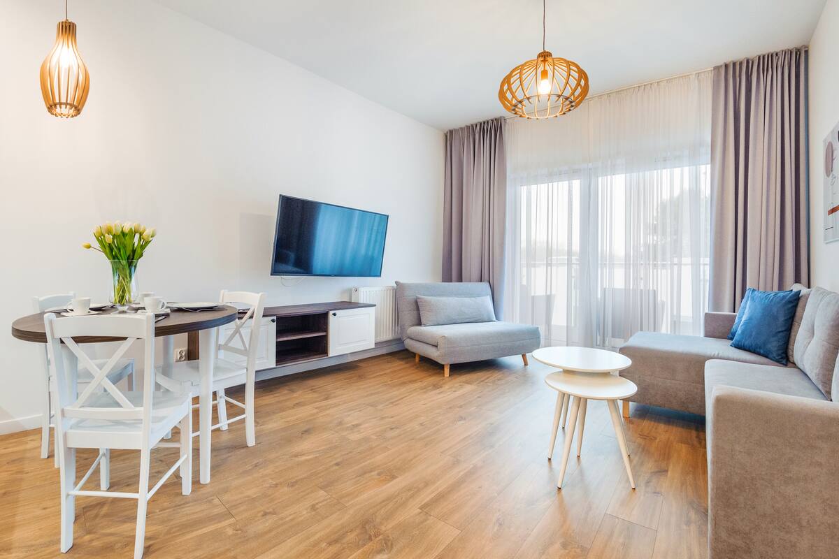 Una sala de estar moderna con comedor, televisor de pantalla plana y un amplio ventanal con cortinas.