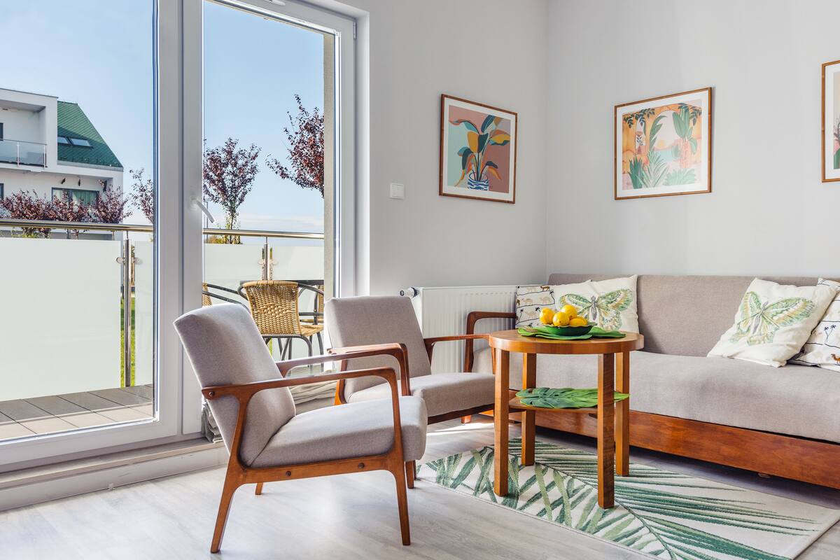 Una sala moderna con un sofá, dos sillones, una mesita con un cuenco de limones y vistas a un balcón con una silla.