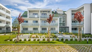Un edificio residencial moderno de varios pisos, con balcones, un jardín ajardinado y un sendero pavimentado.