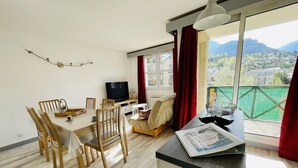 A modern living room with a dining area, a sofa, a TV, and a balcony with a view of the mountains. - Bright 50 M² With Balcony And View On The Valley (Briançon)