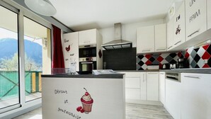 A modern kitchen with white cabinets, a stainless steel range hood, and a view of mountains through a large sliding glass door. - Bright 50 M² With Balcony And View On The Valley (Briançon)
