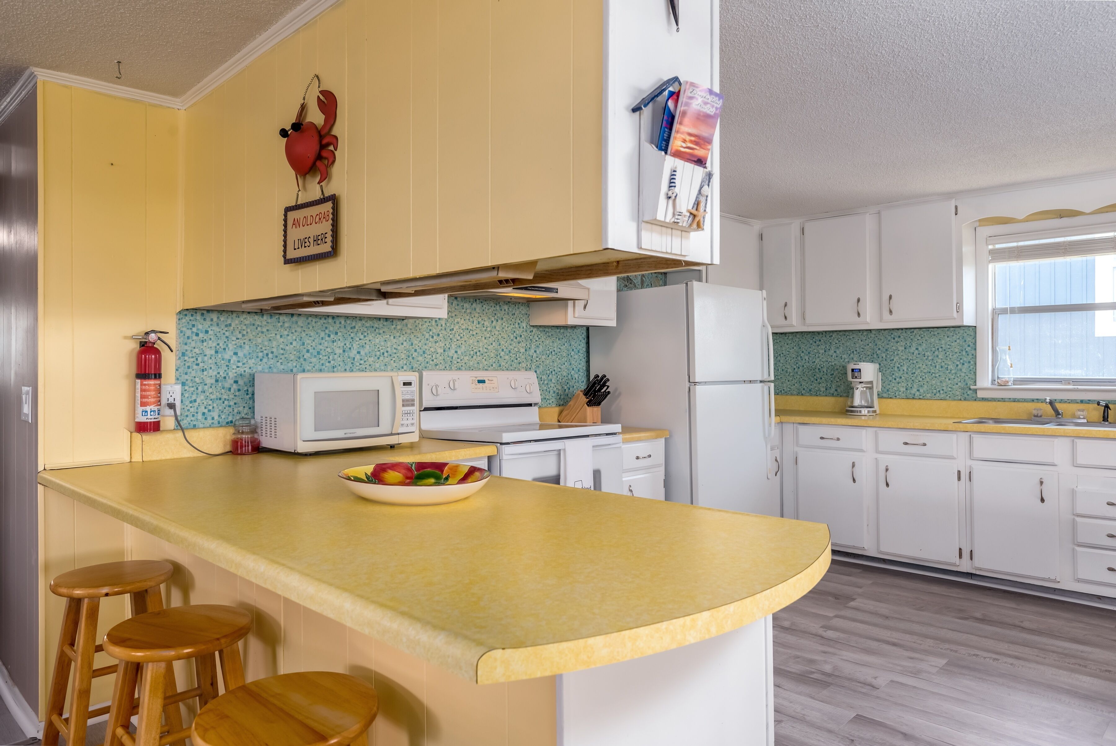 A kitchen with a yellow countertop, white cabinets, a microwave, a stove, and a bowl of fruit.
