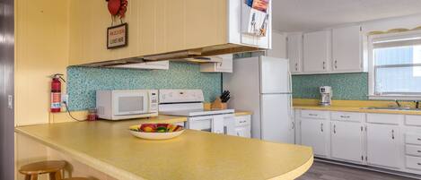 A kitchen with a yellow countertop, white cabinets, a microwave, a stove, and a bowl of fruit.