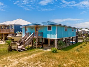Uma casa de dois andares com fachada azul, um deck de madeira e um barco atracado na frente.