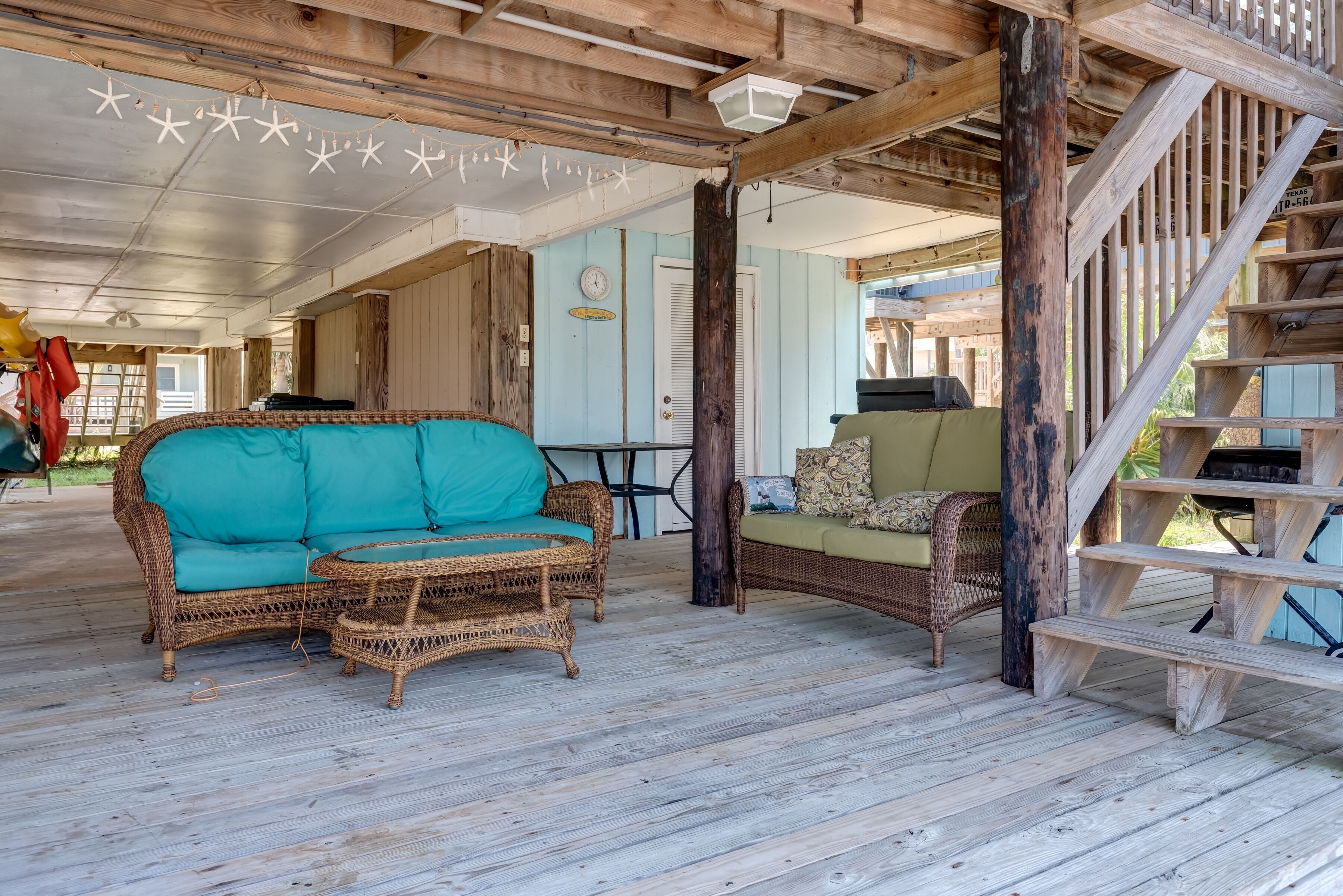 A covered porch with wicker furniture, a wooden staircase, and a clock on the wall.