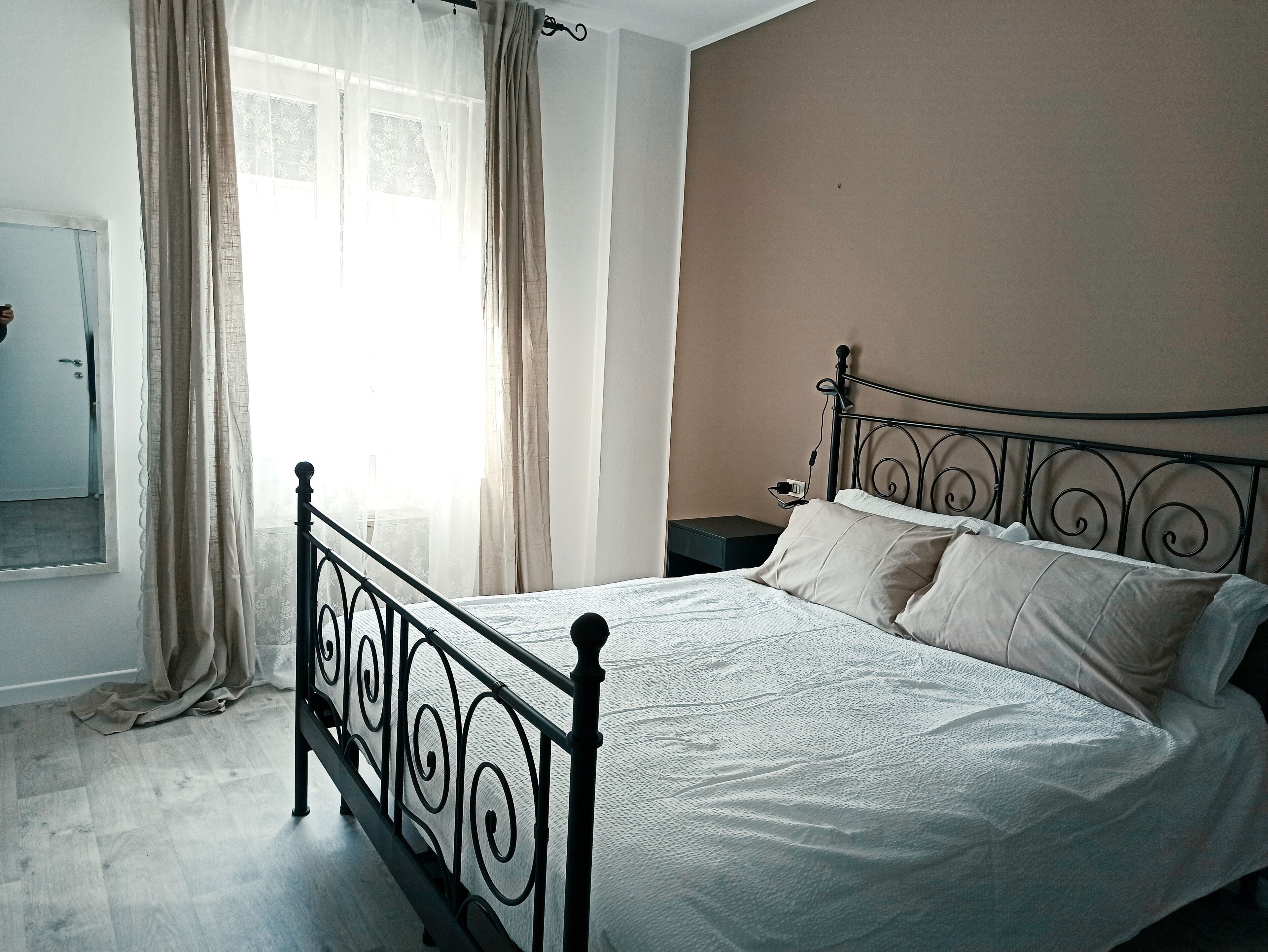 A bedroom with a bed, a nightstand, a window with curtains, and a door.