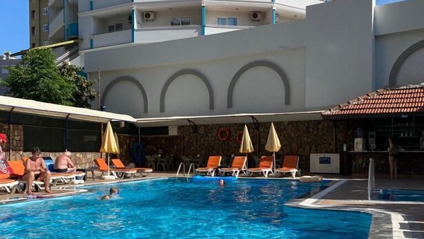 Una piscina con sillas de descanso y sombrillas, rodeada por un edificio con varios balcones.