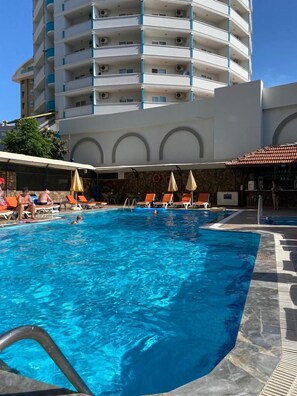 A swimming pool with lounge chairs and umbrellas, surrounded by a building with multiple balconies. - Sun Vera Hotel (Alanya)