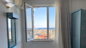 Una habitación con un ventanal grande, una cama, un banco y un armario.