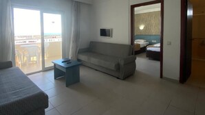 Una habitación de hotel con sofá, una mesita, una cama con cabecera y un ventanal corredero que da a un espacio exterior.