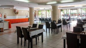 Un amplio comedor interior con varias mesas y sillas, una barra central y grandes ventanales que dejan entrar luz natural.