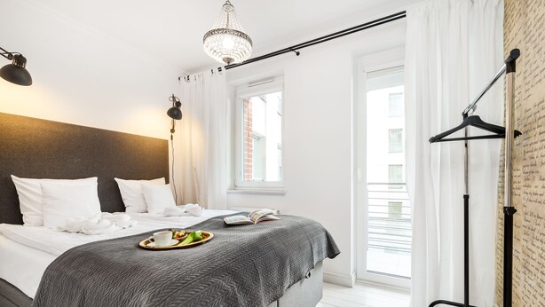 A neatly made bed with a grey quilt, a bedside table with a tray of breakfast items, and a hanging light fixture. - Happy Stay Old Town Tartaczna St. 314 (Gdansk)
