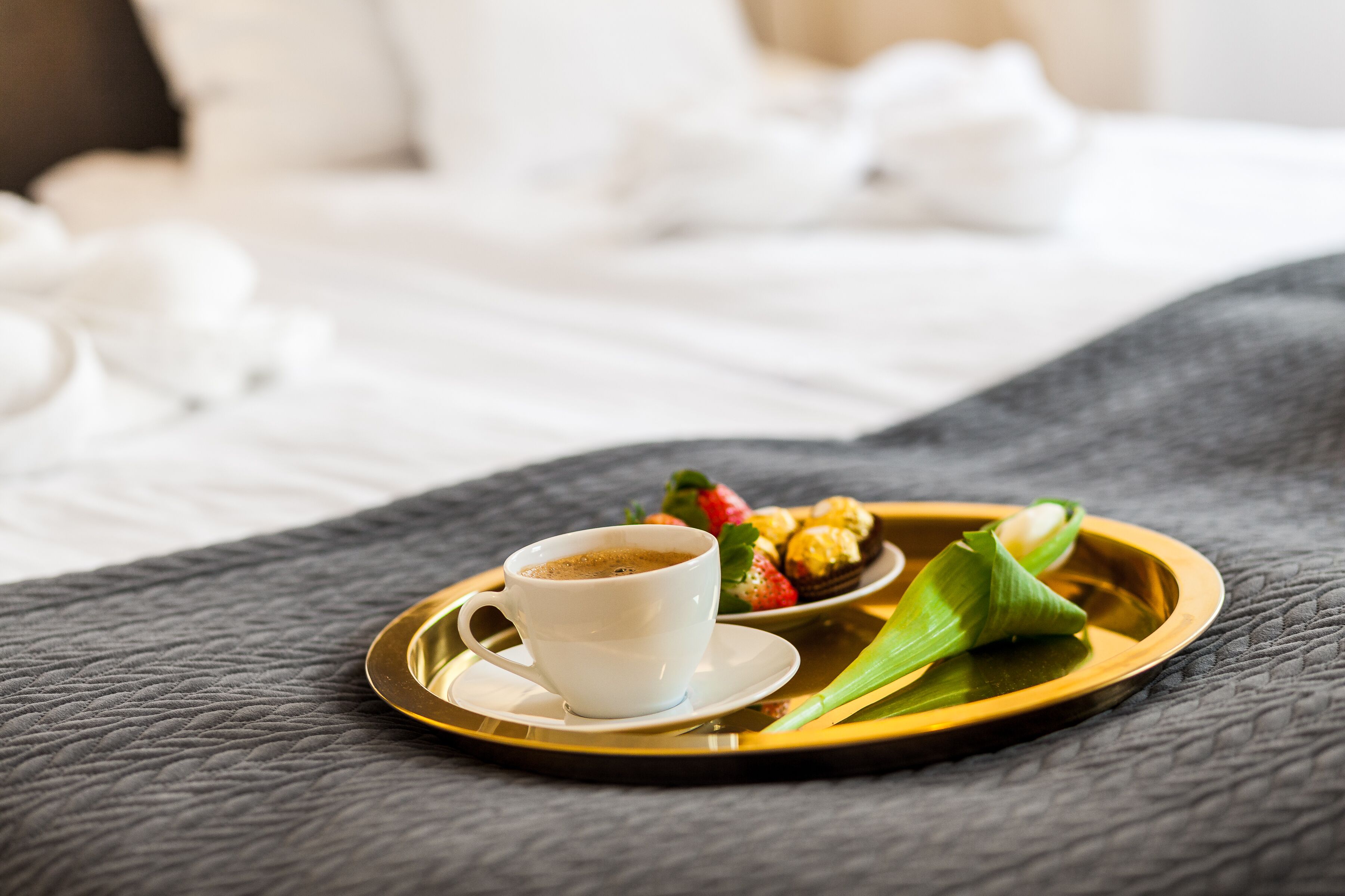 A tray with a cup of coffee, strawberries, and pastries on a bed.