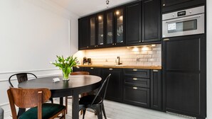 A modern kitchen with dark cabinetry, a white countertop, and a dining area with a round table and chairs. - Happy Stay Old Town Tartaczna St. 314 (Gdansk)