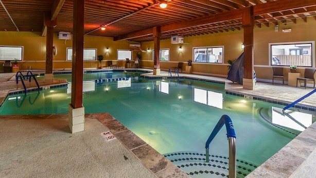 Una piscina interior con agua cristalina, vigas de madera y suelo de baldosas.