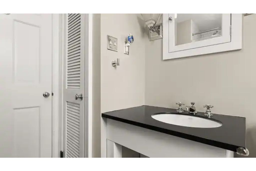 Une salle de bain avec une porte blanche, un lavabo noir et un miroir au-dessus.