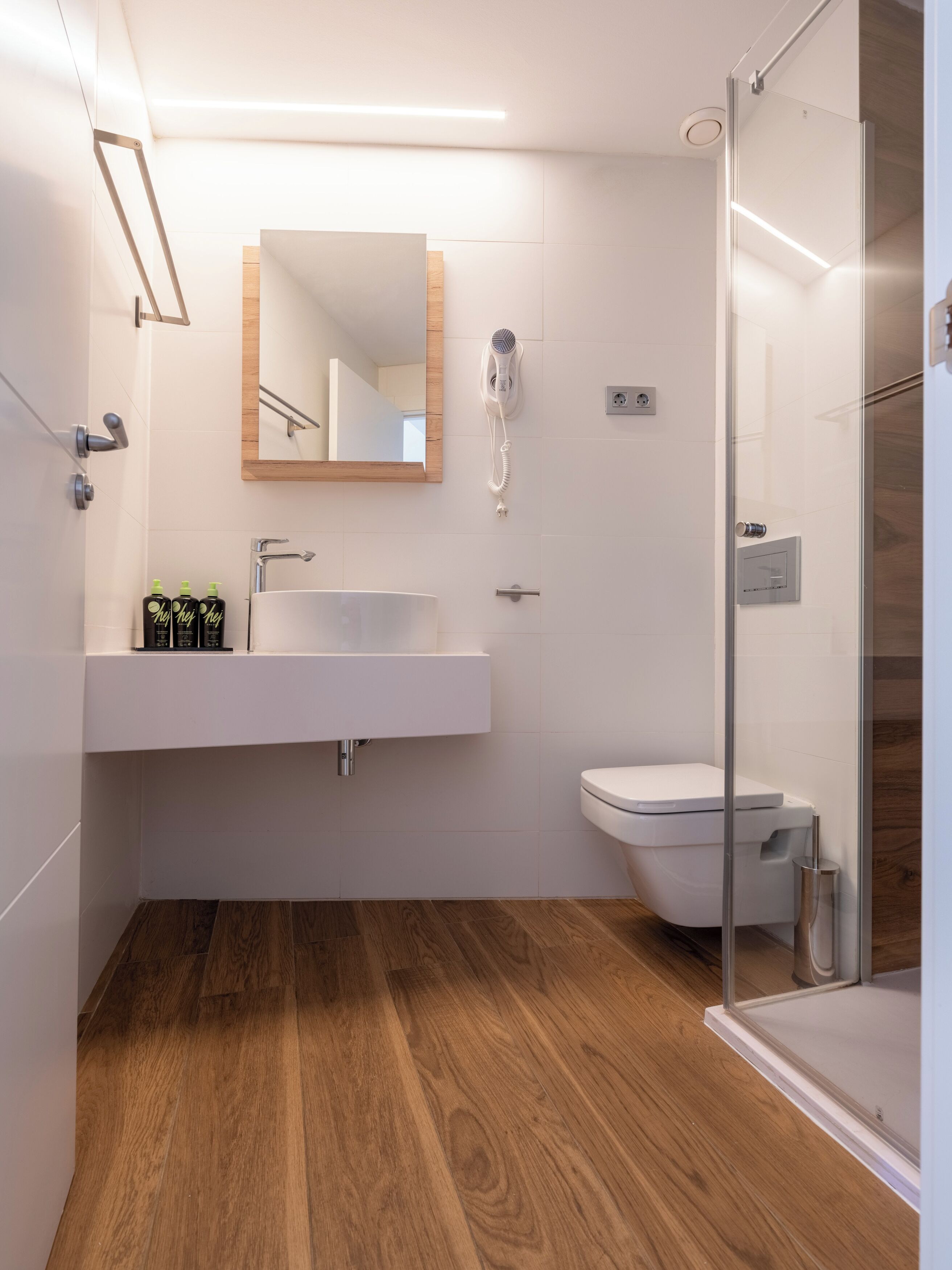 Un bany modern amb terra de fusta, un lavabo blanc, un vàter i una cabina de dutxa de vidre.