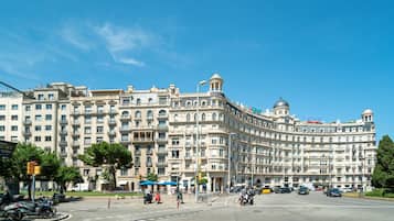 Un edificio grande e histórico con varios balcones y una cúpula, situado en una intersección concurrida con coches y motocicletas.